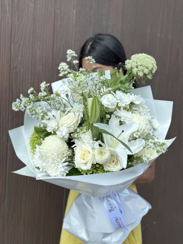 A luxurious all-white bouquet featuring lilies, roses, and chrysanthemums