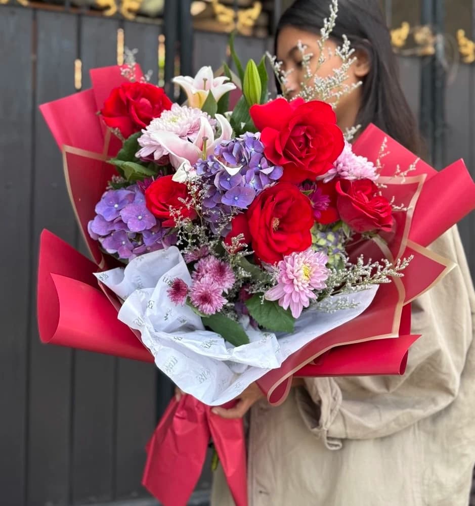 A passionate blend of red roses, purple hydrangeas, and pink blooms wrapped in striking red.